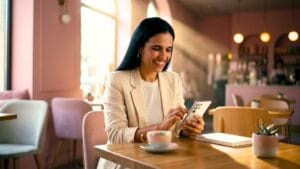 Mulher em uma cafeteria sorrindo enquanto usa o celular para escolher nomes para instagram feminino.
