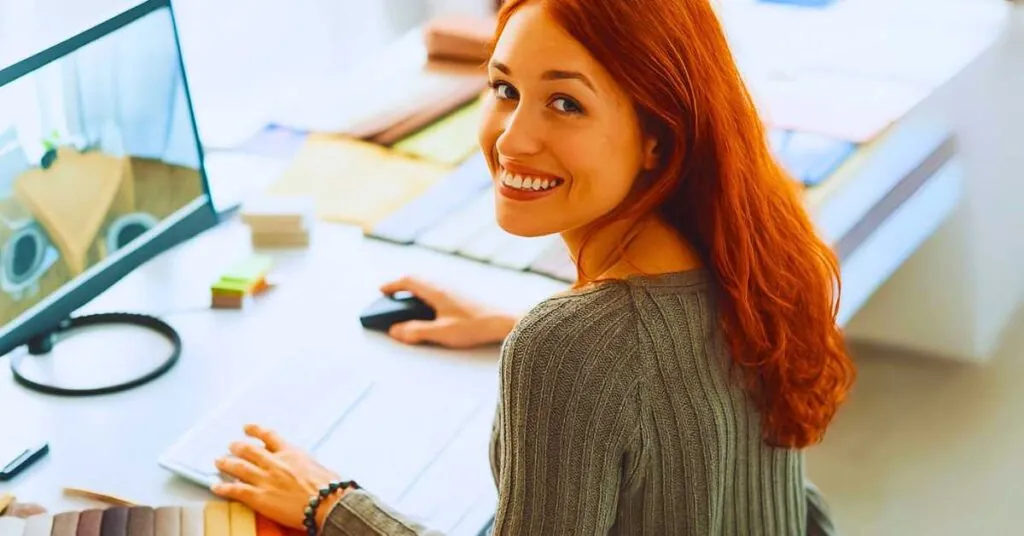 Designer profissional ruiva sorrindo em estúdio de trabalho, representando os melhores cursos para fazer de design de interiores em 2025